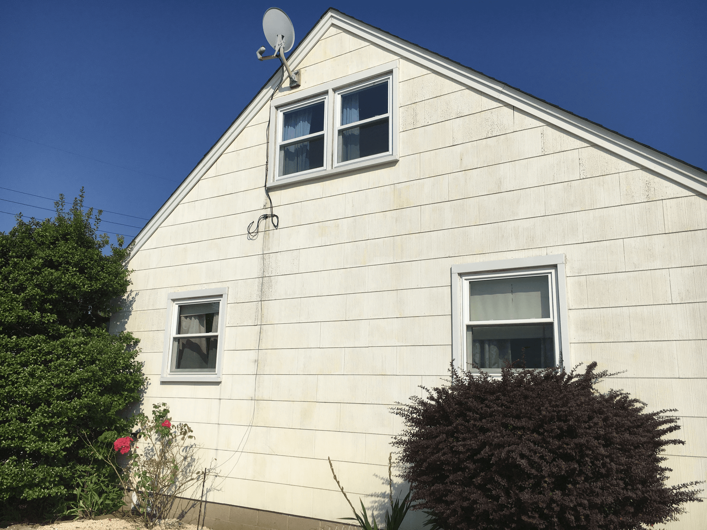 Gable end of a house with weathered cream siding, before painting